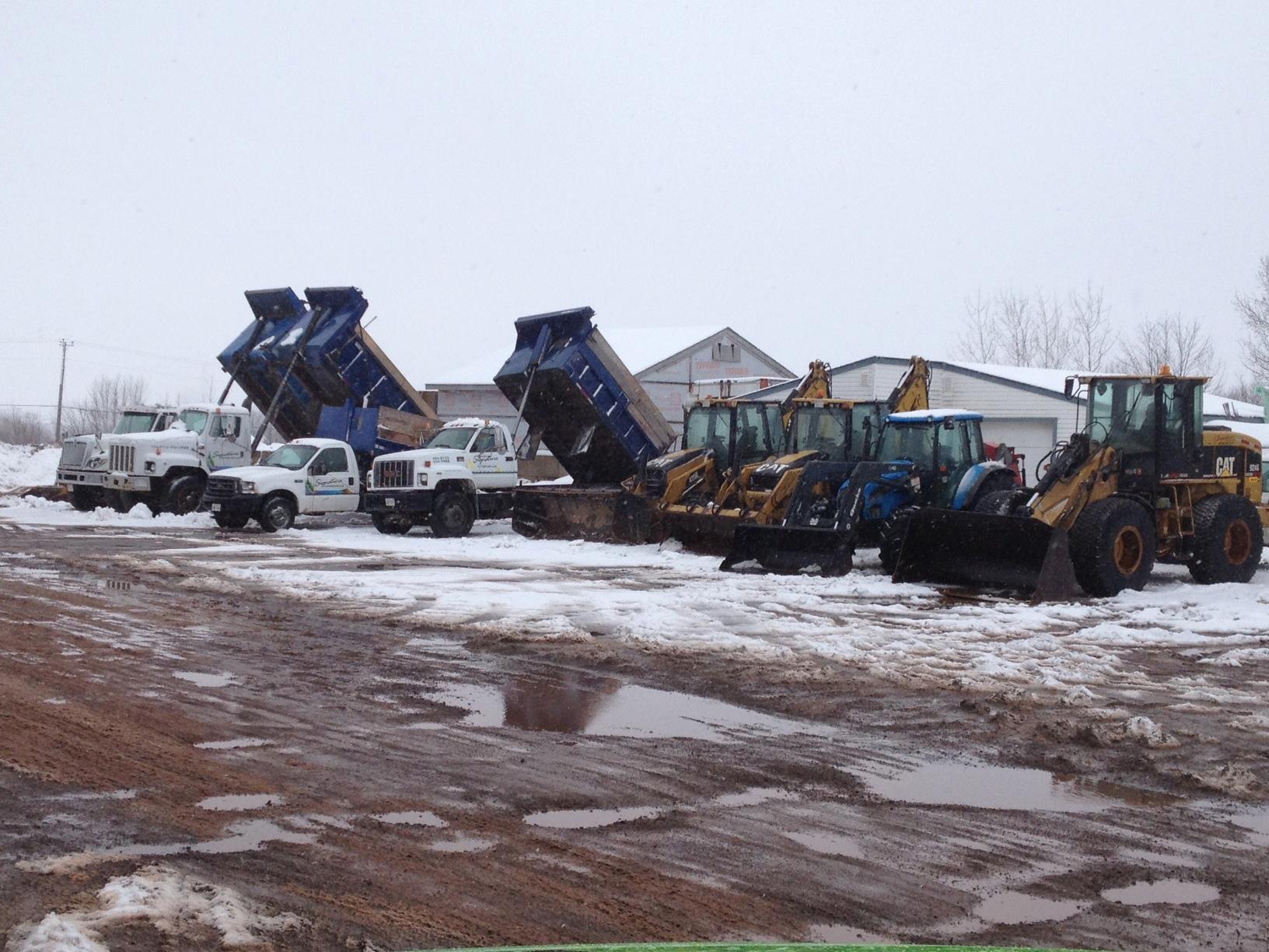 Snow Equipment and Machinery Yard Commercial Snow & Ice Removal Snow-covered yard with lined-up construction vehicles and dump trucks.