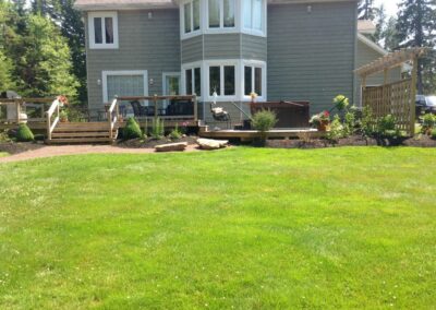Green backyard with wooden deck, hot tub, and landscaped border beds.